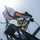 An upward-looking photograph of a ship or vessel's mast structure with multiple flags flying in the wind. The image is taken from below against a bright, hazy sky with visible sun glare causing lens flare. Several nautical signal flags and what appears to be a white flag with a red cross design are prominently displayed.
