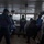 The image shows the bridge/wheelhouse of a naval or coast guard vessel with multiple uniformed personnel present. One individual wearing a high-visibility vest marked 'G.N.S CHENLE' stands at the helm console, looking out toward the water through the forward windows. The scene appears to be an active navigation or operational exercise, with several crew members in blue uniforms and face masks observing.