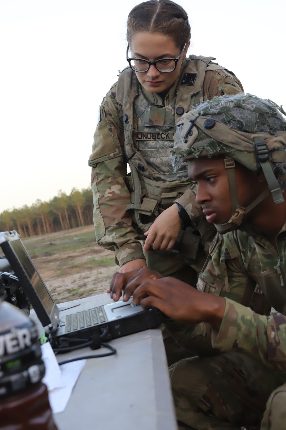 A Lieutenant over looking a shoulder of a Soldier in on a computer controlling the Raven system out in the field at JRTC