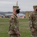 Two U.S. Army soldiers in OCP (Operational Camouflage Pattern) uniforms and black face masks are standing on a grass field, likely at a military installation. The soldier in the foreground is wearing a colorful party hat on top of his patrol cap, suggesting a celebratory occasion. A name tape reading 'STRASSER' is visible on the soldier in the background.