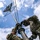 Marines with 3d Supply Battalion demonstrate their field communication capabilities Two U.S. Marines in MARPAT woodland camouflage uniforms are assembling or erecting a communications mast with a parabolic grid antenna at the top. The photo is taken from a low angle looking upward, providing a dramatic perspective of the mast extending into a partly cloudy sky. Multiple guy wires are visible radiating outward from the mast to stabilize the structure.