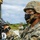 Marines with 3d Supply Battalion demonstrate their field communication capabilities A U.S. Marine in full combat gear is working with what appears to be a mortar system during a training exercise. The Marine is wearing MARPAT digital camouflage, a combat helmet, black face mask, glasses, and black tactical gloves, with a smartwatch visible on the wrist. At least one additional service member is visible in the background.