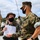 Marines with 3d Supply Battalion demonstrate their field communication capabilities Two U.S. Marines in MARPAT camouflage uniforms and black face masks are engaged in a discussion at what appears to be a field training or operational site. The Marine on the left, wearing a boonie hat, is holding a binder or clipboard with documents. Military vehicles and additional personnel are visible in the background.