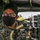 Marines with 3d Supply Battalion demonstrate their field communication capabilities A military service member wearing MARPAT digital camouflage uniform, glasses, and a black face mask is positioned inside what appears to be a military vehicle, likely a HMMWV (Humvee). The individual is in close proximity to mounted equipment, possibly a weapon system or communications device. The setting suggests a training or operational environment.