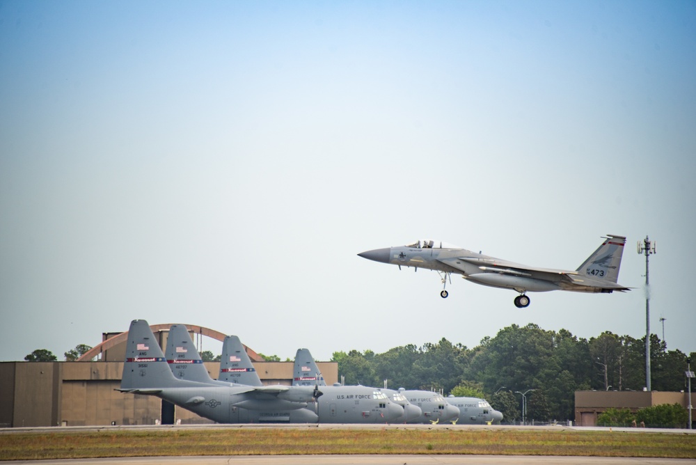 F-15 Eagle passes line full of C-130 Hercules aircraft