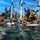 Joint Task Force-Bravo conducts overwater survival training Military personnel are conducting a water-based training exercise in a shallow coastal area. One individual in swim gear is in the water while others in camouflage uniforms and a blue helmet lean over a metal frame structure at the water's surface, appearing to review documents or a map. Additional uniformed personnel observe from the background near a sandy shoreline.