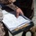 A person in military camouflage uniform is holding a metal clipboard containing what appear to be shooting range scorecards or target assessment forms. The documents show circular target diagrams with scoring grids, consistent with marksmanship qualification paperwork. The setting appears to be outdoors in a sandy or arid environment.