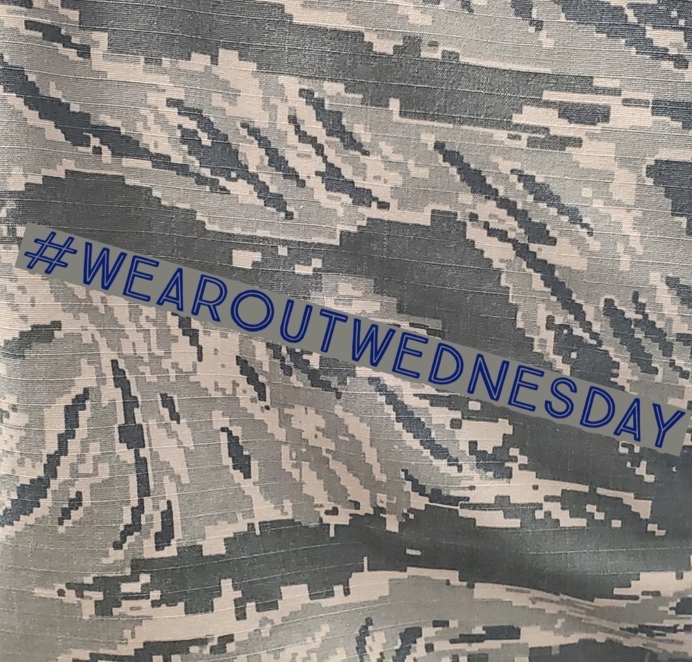 The image shows a close-up of a military digital camouflage fabric, consistent with the U.S. Air Force Airman Battle Uniform (ABU) pattern featuring gray, blue-gray, and tan pixel tones. Overlaid diagonally across the fabric is a semi-transparent banner with the hashtag '#WEAROUTWEDNESDAY' in blue text. This appears to be a social media promotional post related to wearing military uniforms or gear on Wednesdays.