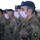A formation of U.S. Army Special Forces (Airborne) soldiers standing at attention while wearing white surgical face masks and black berets. The foreground soldier clearly displays 'Special Forces Airborne' and unit patches on their OCP (Operational Camouflage Pattern) uniform. The image appears to document a military ceremony or formation conducted during a period requiring COVID-19 protective measures.