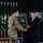 A U.S. Army soldier in MultiCam/OCP uniform is presenting a framed Special Forces commemorative plaque to a civilian man in a dark suit during a formal military ceremony. The framed item features a Green Beret and text reading 'says more about you than you'd ever say about yourself' with 'Special Forces' visible at the bottom. The setting appears to be an official military event with unit flags and insignia displayed in the background.