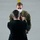 A civilian in a dark suit is pinning a medal or decoration onto the chest of a U.S. Army soldier in OCP (Operational Camouflage Pattern) uniform. The soldier is wearing a white face mask, suggesting this ceremony took place during the COVID-19 pandemic period. This appears to be a formal military awards or decoration ceremony conducted indoors on a concrete floor.