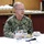 A U.S. Navy officer identified by his name tape as 'Caudle' is seated at a dining table, apparently speaking during a meal or briefing event. A place card in front of him reads 'Vice Admiral Daryl Caudle, Commander, Submarine Forces.' He is wearing Navy Working Uniform (NWU) digital camouflage with U.S. flag patch and submarine warfare insignia.