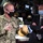 A U.S. Navy officer with the name tag 'CAUDLE' is briefing a civilian official in a dark suit aboard what appears to be a naval vessel's command or control room. Both individuals and others in the background are wearing face masks, suggesting this was taken during the COVID-19 pandemic period. The Navy officer is holding what appears to be a worn military-style cap with gold insignia.