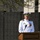 Submarine Squadron Four welcomes new commodore A senior U.S. Navy officer in dress white uniform is delivering a speech at a podium during what appears to be a memorial ceremony. He is surrounded by large black memorial walls engraved with names of fallen service members. The setting suggests a formal military commemoration event, likely held outdoors at a memorial site.