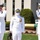 Submarine Squadron Four welcomes new commodore Three U.S. Navy officers in white dress uniforms are participating in a formal military ceremony, likely a change of command. Two officers on the flanks are rendering salutes while the central officer stands at attention. All three are wearing face masks, suggesting the event took place during the COVID-19 pandemic period.