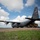 75th EAS Executes Tactical Airlift Mission in Manda Bay, Kenya A U.S. Air Force C-130J Super Hercules military transport aircraft (tail number 83178) assigned to Air Mobility Command (AMC) is parked on an unpaved airstrip with its rear cargo ramp open. A yellow Caterpillar front-end loader/wheel loader is positioned at the rear of the aircraft, suggesting active cargo loading or unloading operations. The scene appears to be at a forward or austere airfield, with temporary structures visible in the background.