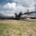 75th EAS Executes Tactical Airlift Mission in Manda Bay, Kenya A U.S. Air Force C-130J Super Hercules military transport aircraft is parked on a tarmac with its propellers spinning, indicating engines are running. Ground crew personnel and support vehicles are visible near the rear of the aircraft, suggesting active loading or unloading operations. The setting appears to be a smaller airfield or forward operating location in a tropical environment.