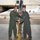 Two U.S. Air Force personnel in olive green flight suits are conducting a guidon/pennant passing ceremony on an aircraft ramp in front of a hangar. A white military jet trainer aircraft is visible in the background with 'TUSKEGEE AIRMEN' written on its fuselage and tail markings 'RA' and '099'. A third person in camouflage uniform is partially visible between the two primary subjects.