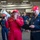 A U.S. Navy personnel member named Garraway, wearing red coveralls, is using a megaphone to address a group in what appears to be a ship's hangar bay. Alongside stands another service member named MacDougall in blue coveralls, reviewing a clipboard. The setting appears to be aboard a naval vessel, likely CVN-77 (USS George H.W. Bush), based on the cap insignia.