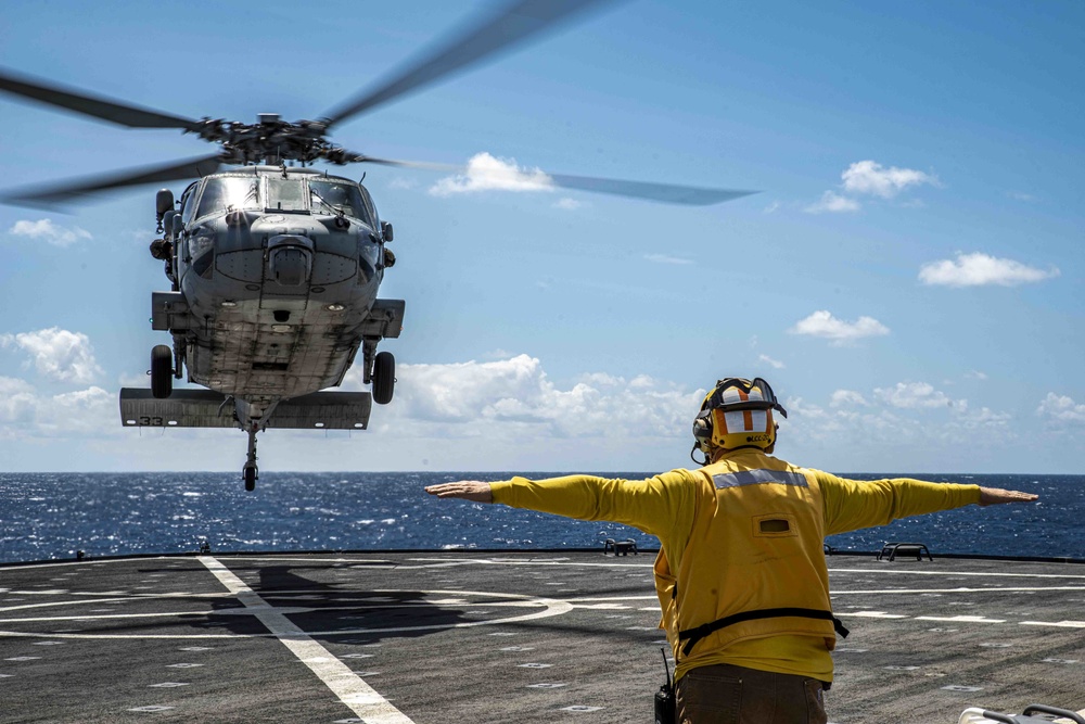 A Military Sealift Command civil service mariner guides an MH-60 Sea Hawk helicopter