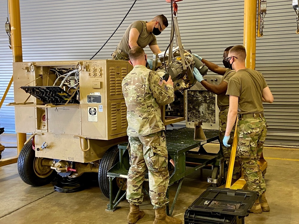 Soldiers hoisting the engine of an Aviation Ground Power Unit (AGPU) off of a maintenance stand.