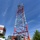 Radio communications tower erected at the 177th Fighter Wing of the New Jersey Air National Guard A red and white lattice communications or navigation tower is being worked on by multiple personnel. Two workers at ground level wearing safety helmets observe while at least two climbers are visible near the upper portion of the tower. The setting appears to be a military or industrial facility with support equipment visible nearby.