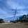 Radio communications tower erected at the 177th Fighter Wing of the New Jersey Air National Guard A large mobile crane is actively lifting a red lattice tower section at what appears to be a military or communications installation. Additional red lattice tower sections are staged horizontally on the ground to the right, awaiting installation. Multiple support vehicles, personnel, and utility infrastructure are visible in the background.