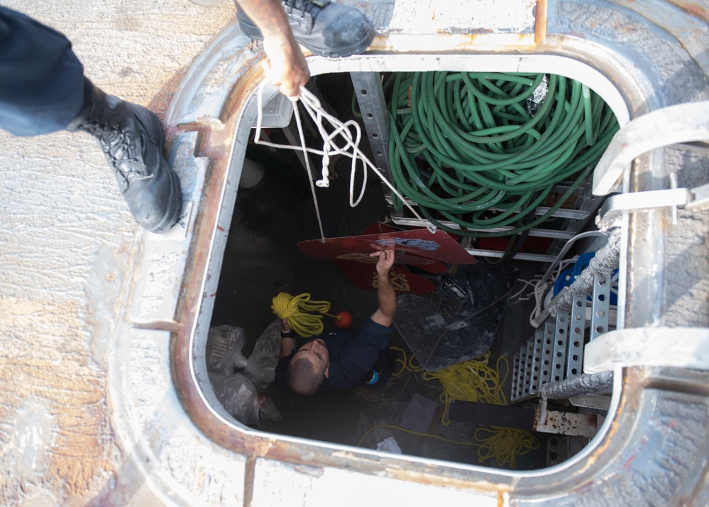 Sailors pass a rat guard through a hatch on the forecastle