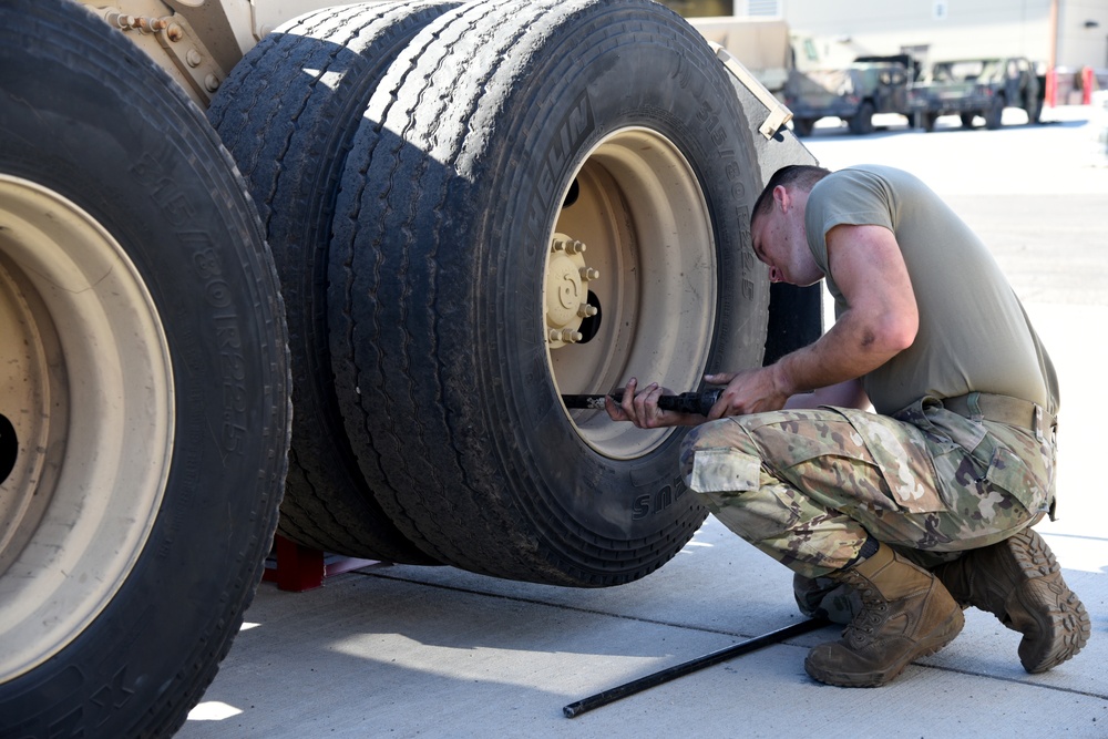 A wheeled vehicle mechanic removes a lug nut from a tire on a M915 truck
