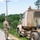 Two U.S. Army soldiers in OCP (Operational Camouflage Pattern) uniforms are positioned alongside a military tan semi-truck (tractor unit) that has pulled off onto the road shoulder. The vehicle bears the markings '207' and '828' and is equipped with air brake lines (green and blue coiled hoses) and an amber warning light on top. The soldiers appear to be conducting a roadside stop or vehicle inspection along a rural road.