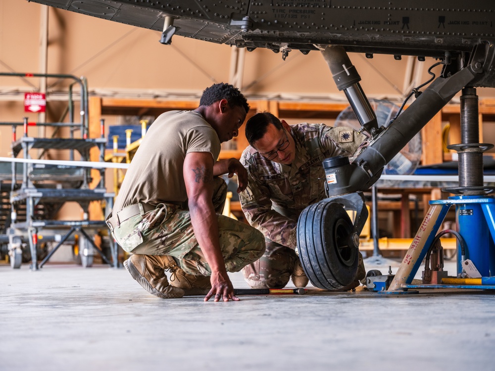 Spc. Tyre Moody, left, and Sgt. Cruz Gonzalez, both 15T UH-60 Black Hawk helicopter technicians from B Company, 640th Aviation Support Battalion, replace a rear tire on a Black Hawk .