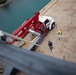 USS Sioux City Sailor Steadies Crane Basket on Ship's Mast While in Port