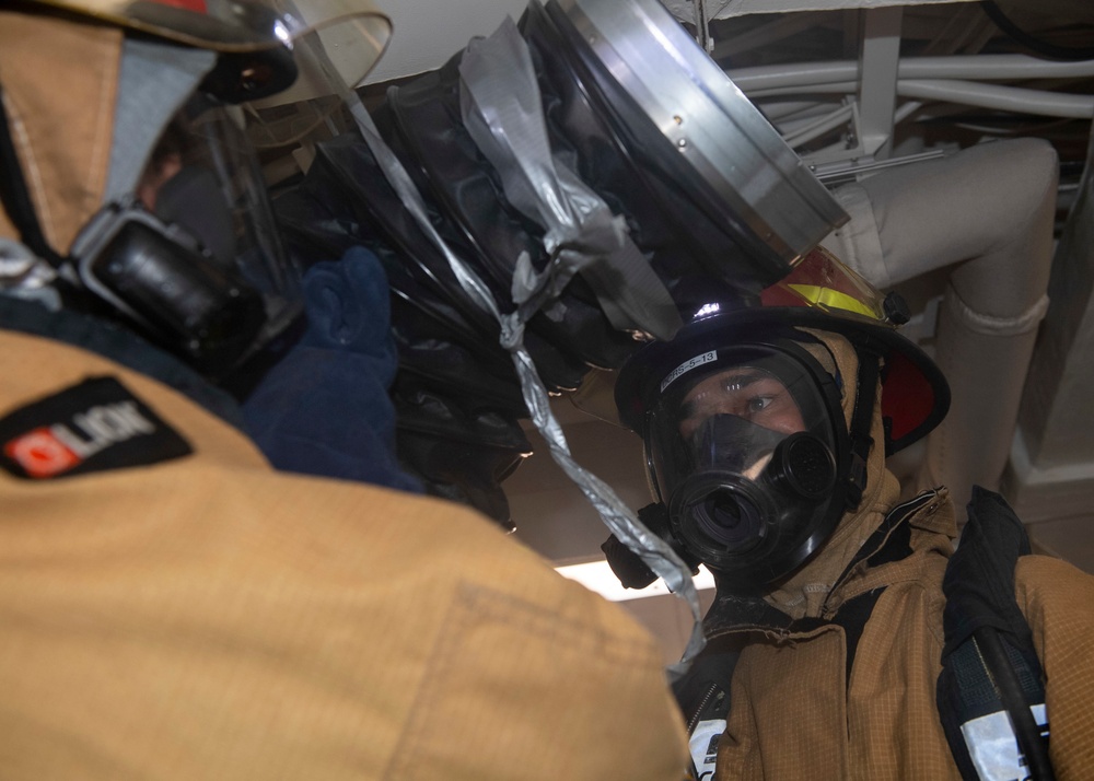 Sailors attach a RAMFAN to a bulkhead to desmoke a space during a firefighting drill