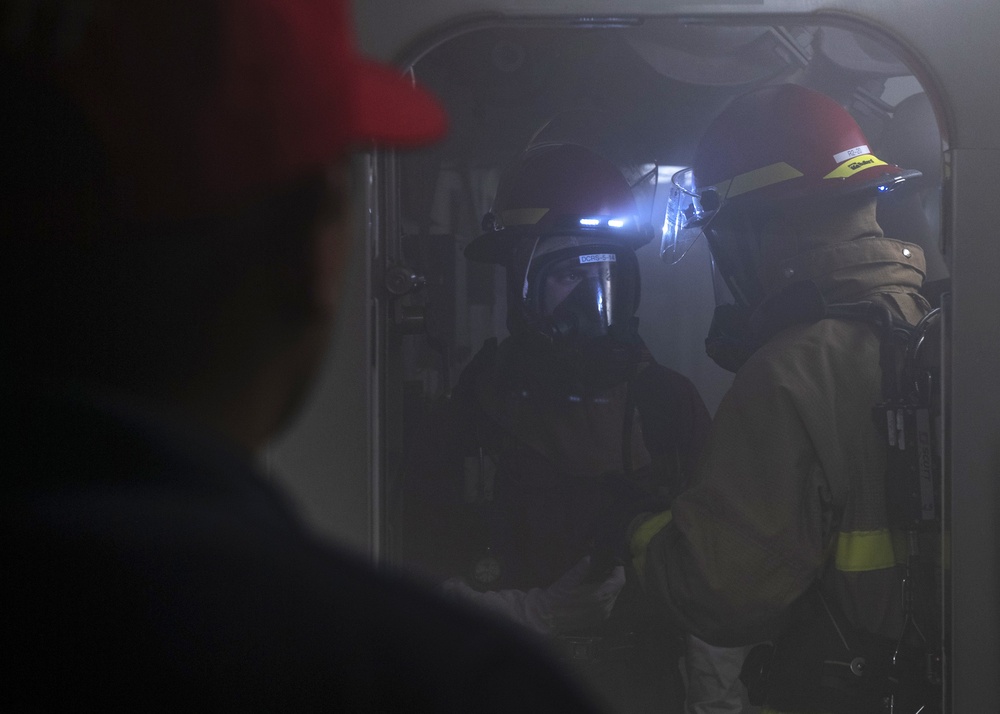 A training team member supervises as Sailors report casualty information during a firefighting drill