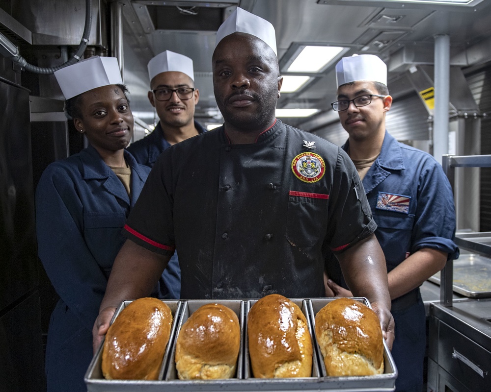Culinary Specialist 3rd Class Marcus Davis presents fresh-baked bread with his culinary team members