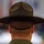 Idaho Youth Challenge Graduates 15th Class The image shows the back of a person wearing a distinctive campaign cover (drill instructor hat) and an olive/green uniform. The wide-brimmed, structured hat is a hallmark of military drill instructors or park rangers. The subject is facing away from the camera toward a blurred background.