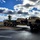 1041st Transportation Company regains identity during eventful annual training A military flatbed transport truck is carrying two tan/desert-colored HMMWVs (Humvees) on a low-boy trailer through what appears to be a military installation or base. The heavy equipment transporter is navigating a roundabout or curved road junction under a dramatic partly cloudy sky. The scene suggests routine military vehicle transport or repositioning operations.