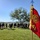 1041st Transportation Company regains identity during eventful annual training A military guidon flag is prominently displayed in the foreground, showing a red pennant with the number '41' and a winged emblem in gold, along with a yellow streamer reading 'Excellence in Retention FY20'. In the blurred background, a large group of personnel dressed in black physical training (PT) uniforms are gathered on a grass field near a tree. The setting appears to be an outdoor military formation or physical training event on a clear, sunny day.