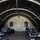 The image shows the interior of a military field operations tent with an arched, tunnel-like structure. Several military personnel in olive drab uniforms are seated at folding tables working on laptops and paperwork. The setting appears to be a temporary command or administrative post, with one individual wearing a face mask.