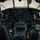 Connecticut Guard upgrades C-130H fleet This image shows the interior cockpit of a large military transport aircraft, likely a C-130 Hercules, viewed from behind the pilot seats looking forward through the windscreen. The cockpit features an extensive array of analog and some digital instruments, throttle quadrants, and dual flight controls. Military personnel are visible on the tarmac outside through the cockpit windows.