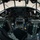 Connecticut Guard upgrades C-130H fleet The image shows the interior cockpit of a large military transport aircraft, likely a C-130 Hercules or similar multi-engine turboprop. The cockpit features dual pilot stations with analog and some digital instrumentation, a central throttle quadrant, and numerous control panels. The aircraft appears to be parked on a tarmac, with ground personnel visible through the windscreen.