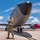 A U.S. Air Force service member in OCP (Operational Camouflage Pattern) uniform stands with arms crossed in front of a KC-135 Stratotanker aircraft on a flight line. The aircraft bears markings indicating serial number 0103, assigned to the 6th Air Refueling Wing (6 ARW) and 927th Air Refueling Wing (927 ARW), suggesting a co-assignment at MacDill Air Force Base, Florida. The photo appears to be a professional or commemorative portrait taken on a sunny day with partial cloud cover.
