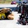 Firefighting gear is laid out on a paved surface, including a yellow helmet, turnout gear, and multiple SCBA (Self-Contained Breathing Apparatus) units with Scott brand air cylinders. The helmet bears text reading 'MCIPAC FESJ, OKINAWA, YAMAUCHI,' indicating a military or Japanese fire service affiliation. The equipment appears staged for a training exercise or pre-deployment readiness check.