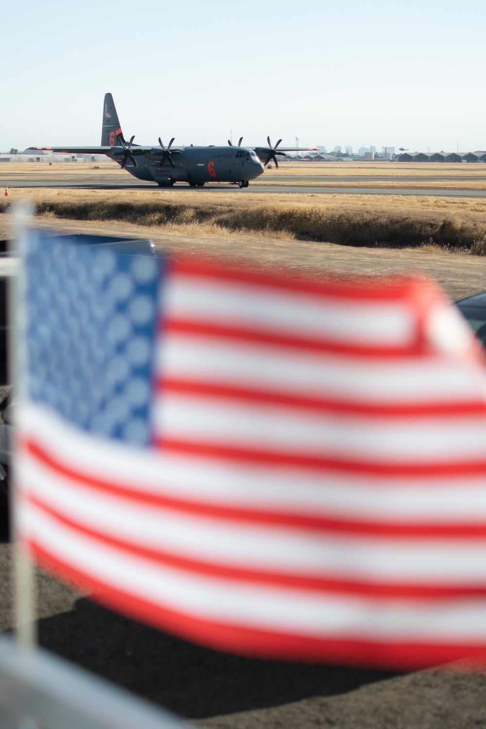 A California Air National Guard C-130 taxis to the runway at McClellan Air Tanker Base, Sacramento, Calif. as the U.S. Flag waves in the wind