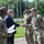 Acting SecAF Roth visits Joint Base Andrews A civilian in a business suit is shaking hands with a uniformed military service member in an outdoor setting. Multiple personnel in OCP (Operational Camouflage Pattern) uniforms are present, suggesting a formal greeting or recognition ceremony. The setting appears to be a military installation with flagpoles and manicured grounds visible in the background.