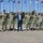 Acting SecAF Roth visits Joint Base Andrews A group of seven military personnel in camouflage uniforms and one civilian in a business suit are posed for a formal group photograph on a circular brick plaza. They are standing in front of a large array of flagpoles displaying what appear to be U.S. state and territory flags. The setting appears to be a military installation or government facility.