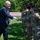 Acting SecAF Roth visits Joint Base Andrews A civilian man in a dark suit is shaking hands with a female military service member in OCP (Operational Camouflage Pattern) uniform outdoors on a grassy area. Two additional service members in matching uniforms and black berets stand in the background. The setting appears to be a formal greeting or recognition ceremony at a military installation.
