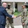 Acting SecAF Roth visits Joint Base Andrews A civilian in a dark pinstripe suit is shaking hands with a military service member in OCP (Operational Camouflage Pattern) uniform during what appears to be an official greeting or reception. Three military personnel in matching camouflage uniforms are present, with one smiling in the background. The setting appears to be outside a military installation or government building.