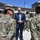 Acting SecAF Roth visits Joint Base Andrews A civilian official in a dark suit is engaged in conversation with multiple military personnel wearing OCP (Operational Camouflage Pattern) uniforms outdoors at what appears to be a military installation. The setting suggests an official visit or inspection, with several service members gathered around the central figures. A photographer in the background is documenting the event.