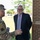 Acting SecAF Roth visits Joint Base Andrews Three individuals are engaged in a friendly conversation outside a brick building on what appears to be a military installation. Two are in military uniform — one in Army OCP camouflage and one in Air Force service dress — while the third is a civilian in a dark suit with a striped shirt and tie. The atmosphere is relaxed and cordial, with all three smiling.